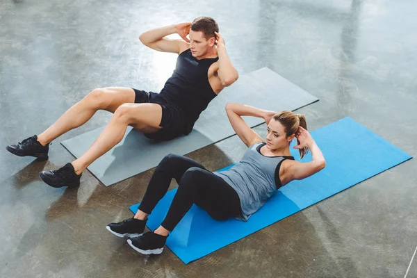 Vista de ángulo alto de la joven pareja deportiva haciendo ejercicios abdominales en el gimnasio - foto de stock