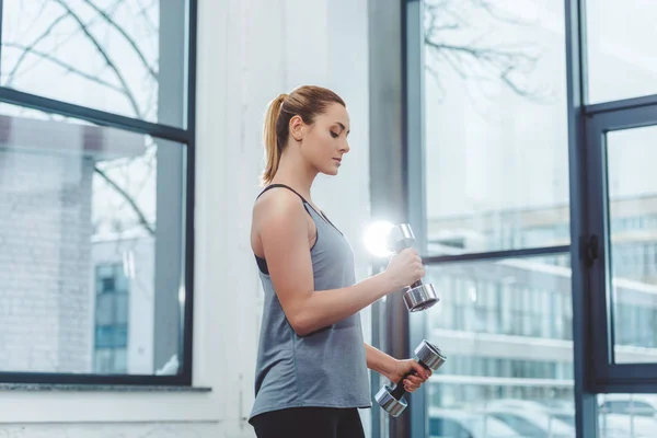 Vue latérale de la formation sportive des jeunes femmes avec haltères dans le studio de fitness — Photo de stock