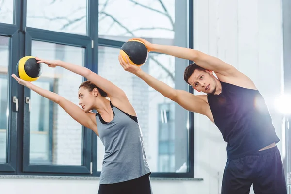 Joven pareja deportiva sosteniendo bolas y entrenando juntos en el gimnasio - foto de stock