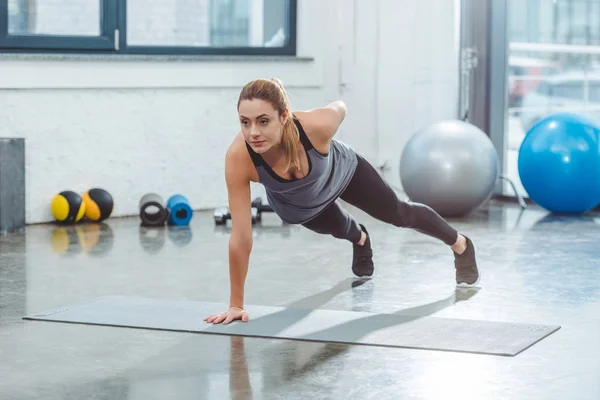 Спортивная юная спортсменка, занимающаяся на коврике для йоги в спортзале — стоковое фото