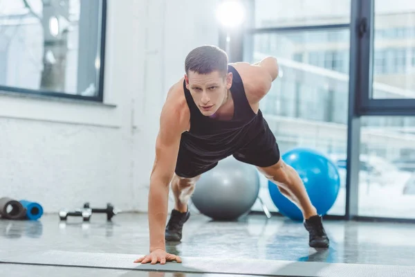 Handsome young sportsman doing push ups on yoga mat — Stock Photo