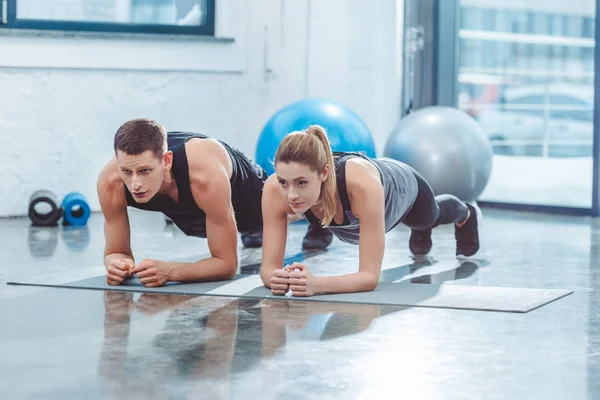 Deportista joven pareja haciendo tablón ejercicio en gimnasio - foto de stock