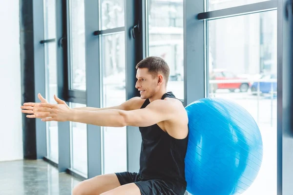 Вид сбоку улыбающийся спортсмен упражняющийся с фитнес-мячом в тренажерном зале — стоковое фото