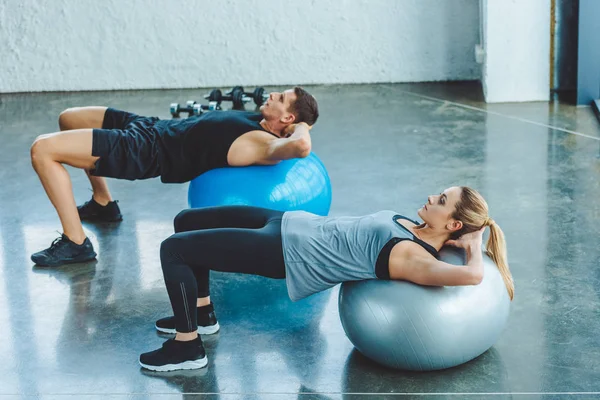 Jovem homem e mulher se exercitando em bolas de fitness no ginásio — Fotografia de Stock