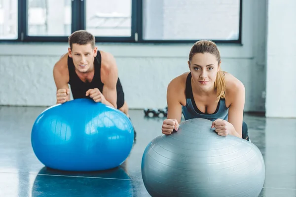 Jovem homem e mulher se exercitando em bolas de fitness no ginásio — Fotografia de Stock