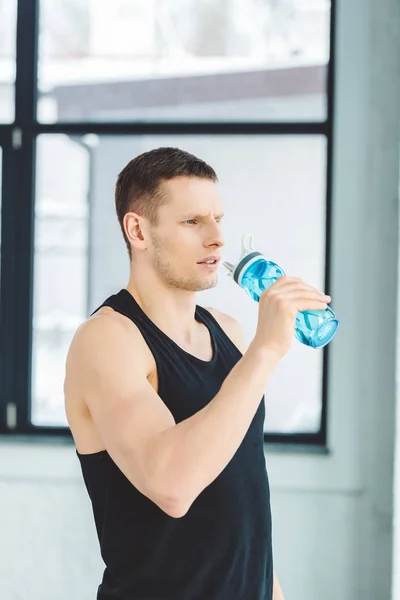 Retrato del deportista bebiendo agua de la botella deportiva después de entrenar en el gimnasio - foto de stock