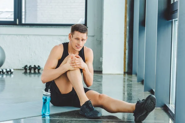 Sportif avec genou blessé reposant sur le tapis dans la salle de gym — Photo de stock