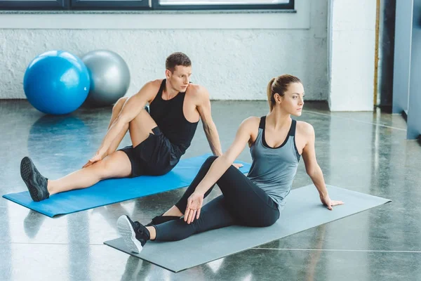 Pareja estiramiento en esteras antes del entrenamiento en el gimnasio - foto de stock