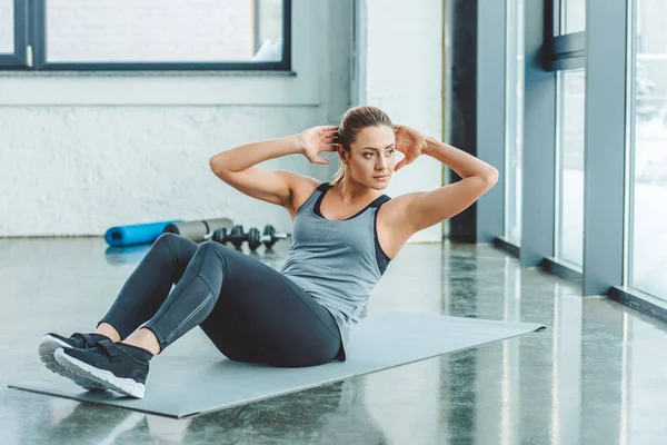 Молодая спортсменка делает упражнения на прессе на коврике в спортзале — стоковое фото