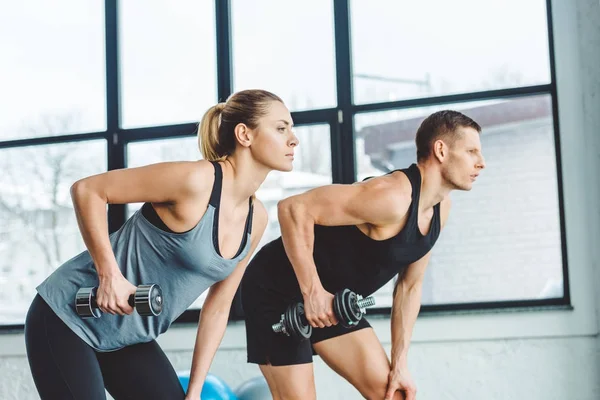 Vista lateral de pareja en entrenamiento de ropa deportiva con mancuernas en gimnasio - foto de stock