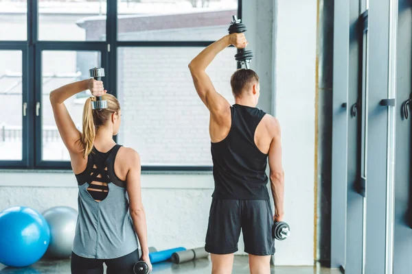 Vista trasera de pareja en entrenamiento de ropa deportiva con mancuernas en gimnasio - foto de stock