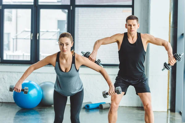 Couple concentré dans l'entraînement de vêtements de sport avec haltères dans la salle de gym — Photo de stock