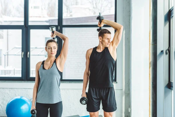 Couple en entraînement de vêtements de sport avec haltères dans la salle de gym — Photo de stock