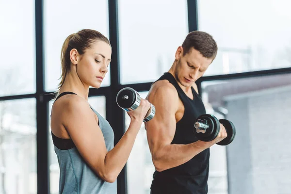 Vista laterale di coppia in allenamento di abbigliamento sportivo con manubri in palestra — Foto stock