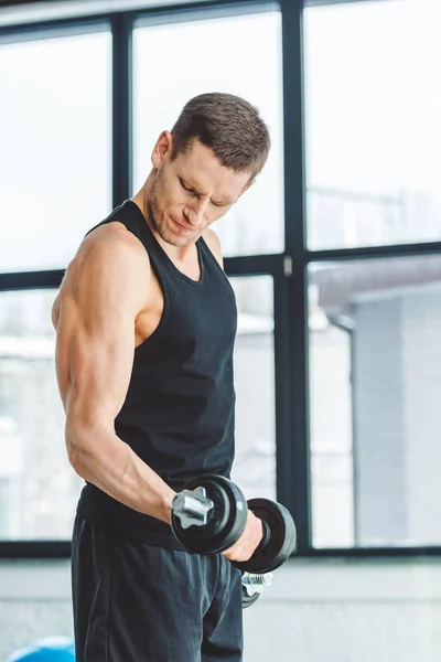 Vue latérale du jeune sportif travaillant avec des haltères dans la salle de gym — Photo de stock