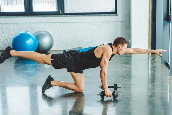 Vue latérale du jeune sportif travaillant avec des haltères dans la salle de gym — Photo de stock