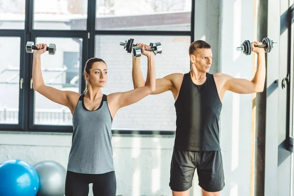 Concentré jeune homme et femme exercice avec haltères dans la salle de gym — Photo de stock