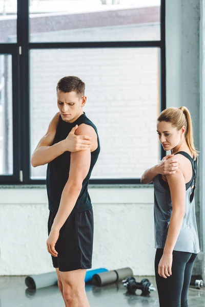 Pareja joven estirándose antes del entrenamiento en el gimnasio - foto de stock