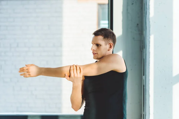 Vista laterale del giovane che si allunga prima dell'allenamento in palestra — Foto stock