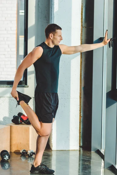 Side view of young man stretching before workout in gym — Stock Photo