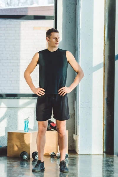 Jeune sportif akimbo en vêtements de sport debout dans la salle de gym — Photo de stock