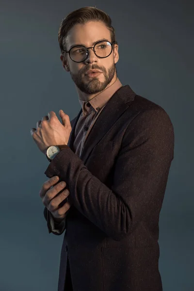 Homem barbudo elegante bonito em relógio de pulso e óculos olhando para longe isolado em cinza — Fotografia de Stock