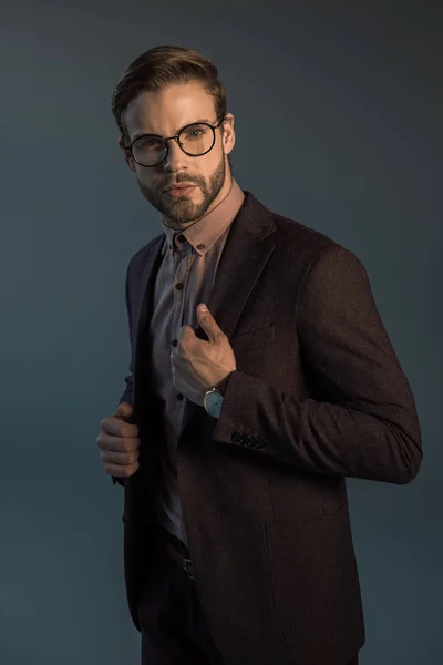 Bel homme barbu élégant en montre-bracelet et lunettes regardant la caméra isolée sur gris — Photo de stock