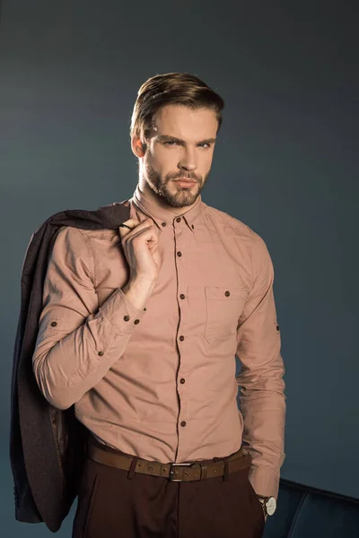 Portrait of handsome young businessman holding suit jacket and looking at camera isolated on grey — Stock Photo