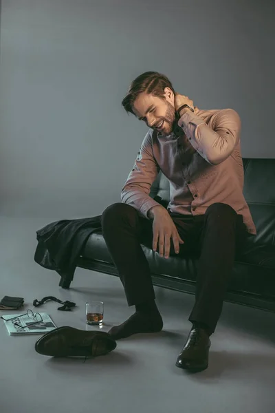 Молодий бізнесмен, який страждає від болю в шиї, сидячи на дивані — стокове фото