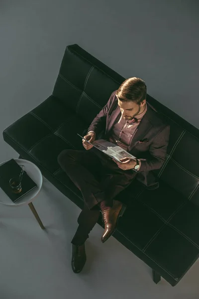 Vista de ángulo alto del joven empresario leyendo el periódico mientras está sentado en el sofá - foto de stock