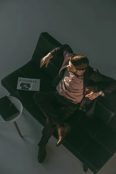 Vue grand angle du jeune homme buvant du whisky et regardant loin tout en étant assis sur le canapé — Photo de stock