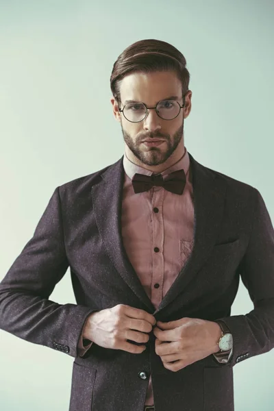 Retrato de joven hombre de negocios guapo abotonando chaqueta traje de moda y mirando a la cámara aislada en gris - foto de stock