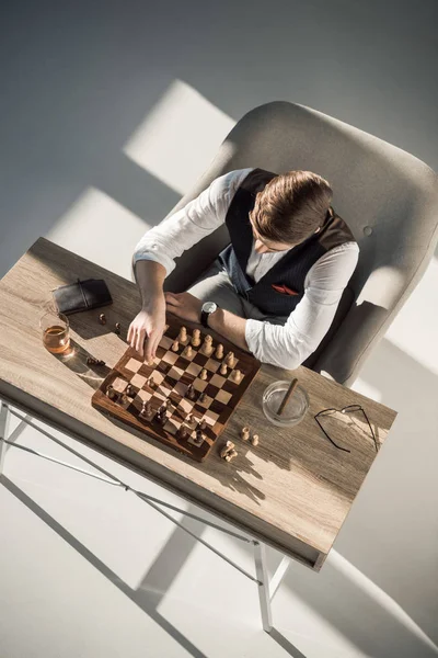 Vista aérea del hombre de negocios jugando al ajedrez mientras bebe whisky y fuma cigarro - foto de stock