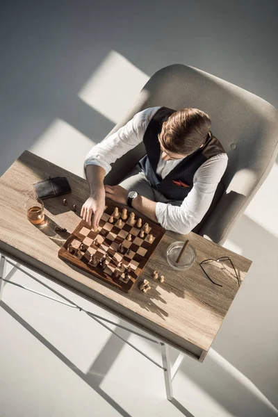 Vue aérienne d'un homme d'affaires jouant aux échecs tout en buvant du whisky et en fumant un cigare — Photo de stock