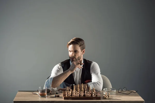 Joven y elegante hombre de negocios con cigarro mirando hacia otro lado mientras juega al ajedrez — Stock Photo