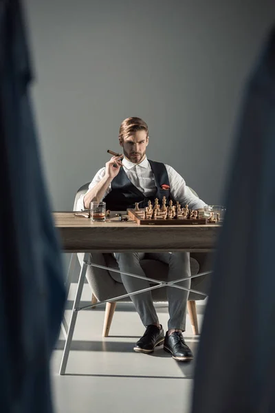 Enfoque selectivo de joven empresario con cigarro mirando a la cámara mientras juega al ajedrez - foto de stock