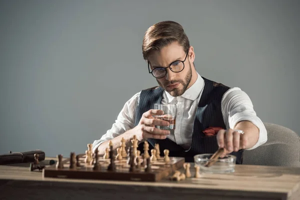 Young businessman with glass of whisky and cigar playing chess — Stock Photo