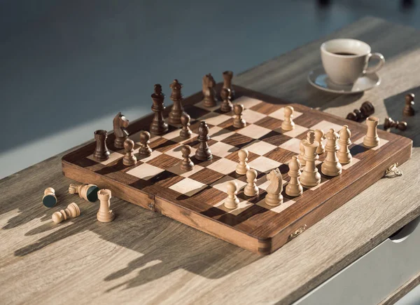 Крупним планом шахова дошка з шматочками і чашкою кави на дерев'яному столі — стокове фото