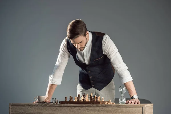 Focado barbudo homem elegante olhando para tabuleiro de xadrez com figuras — Fotografia de Stock