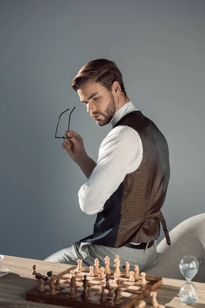 Joven y elegante hombre de negocios con gafas y mirando al tablero de ajedrez — Stock Photo