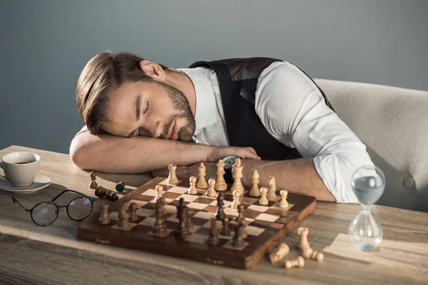 Apuesto joven empresario durmiendo en la mesa con tablero de ajedrez - foto de stock