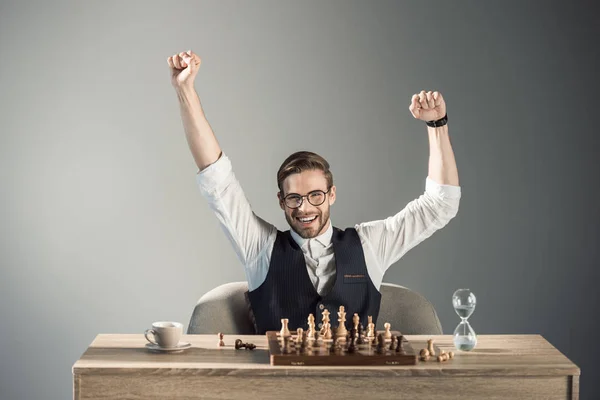 Triunfante joven hombre de negocios en gafas sonriendo a la cámara mientras juega al ajedrez - foto de stock
