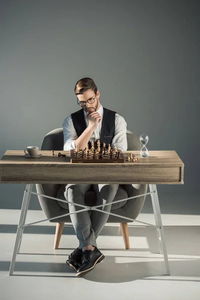 Pensativo joven hombre de negocios en gafas jugando ajedrez - foto de stock