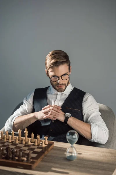 Concentrated young businessman looking at sand clock while playing chess — Stock Photo