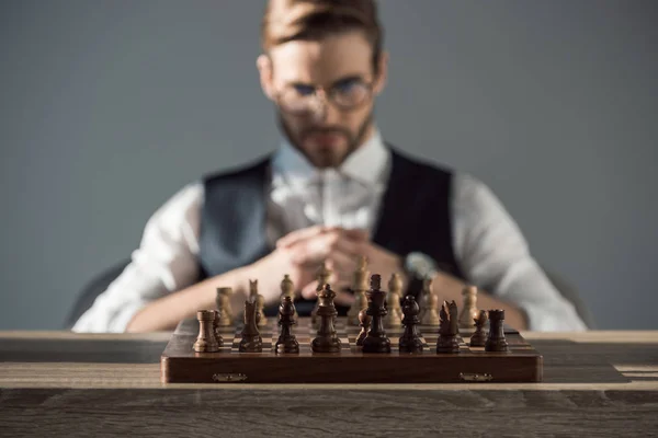 Close-up view of chess board with pieces and young businessman behind — Stock Photo