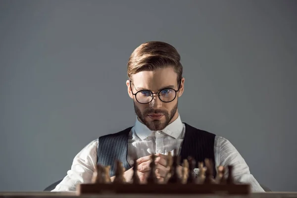 Foyer sélectif de jeune homme d'affaires dans les lunettes regardant l'échiquier avec des morceaux — Photo de stock