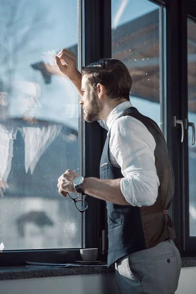 Portrait of stylish young businessman holding eyeglasses and looking at window — Stock Photo