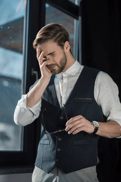 Portrait of young tired businessman with closed eyes holding eyeglasses — Stock Photo