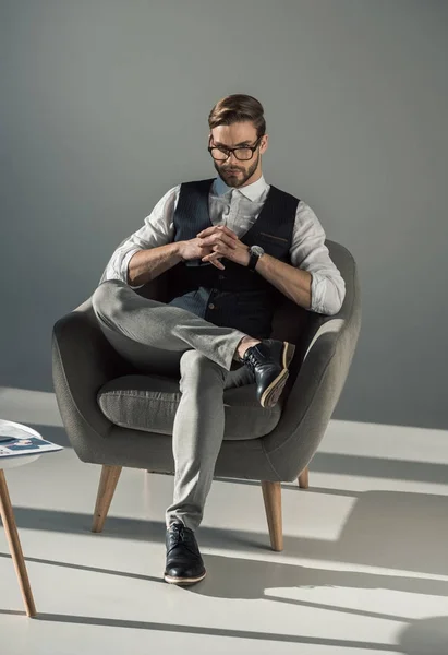 Handsome stylish young businessman in eyeglasses sitting on armchair — Stock Photo