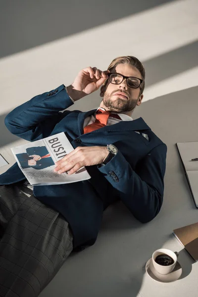 Vue grand angle de beau jeune homme d'affaires élégant avec journal couché sur le sol — Photo de stock